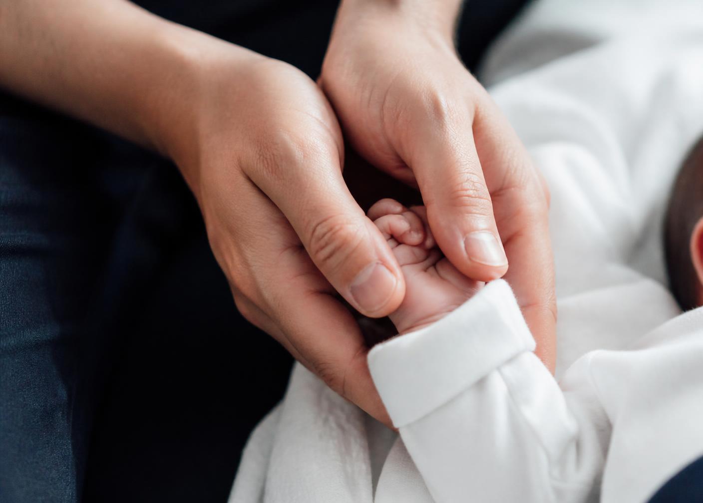 Le mani di un genitore che tengono la mano di un neonato